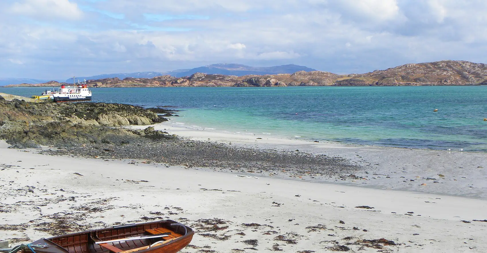 Spiaggia di sabbia bianca e acqua verde-azzurra sul Sound of Iona, con una barca tirata in secca